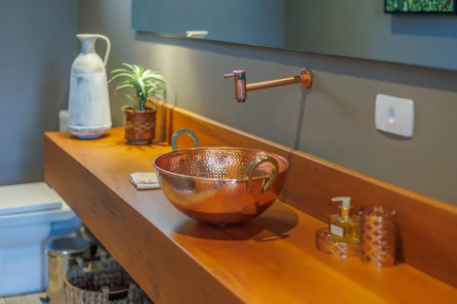 Cuba de cobre sobre bancada de madeira no lavabo
